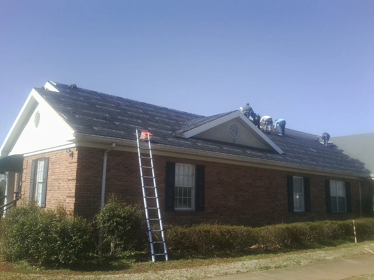 Crew tearing shingles off a brick ranch roof with a ladder set — Metal Roof Repair work by our crew in Quinault