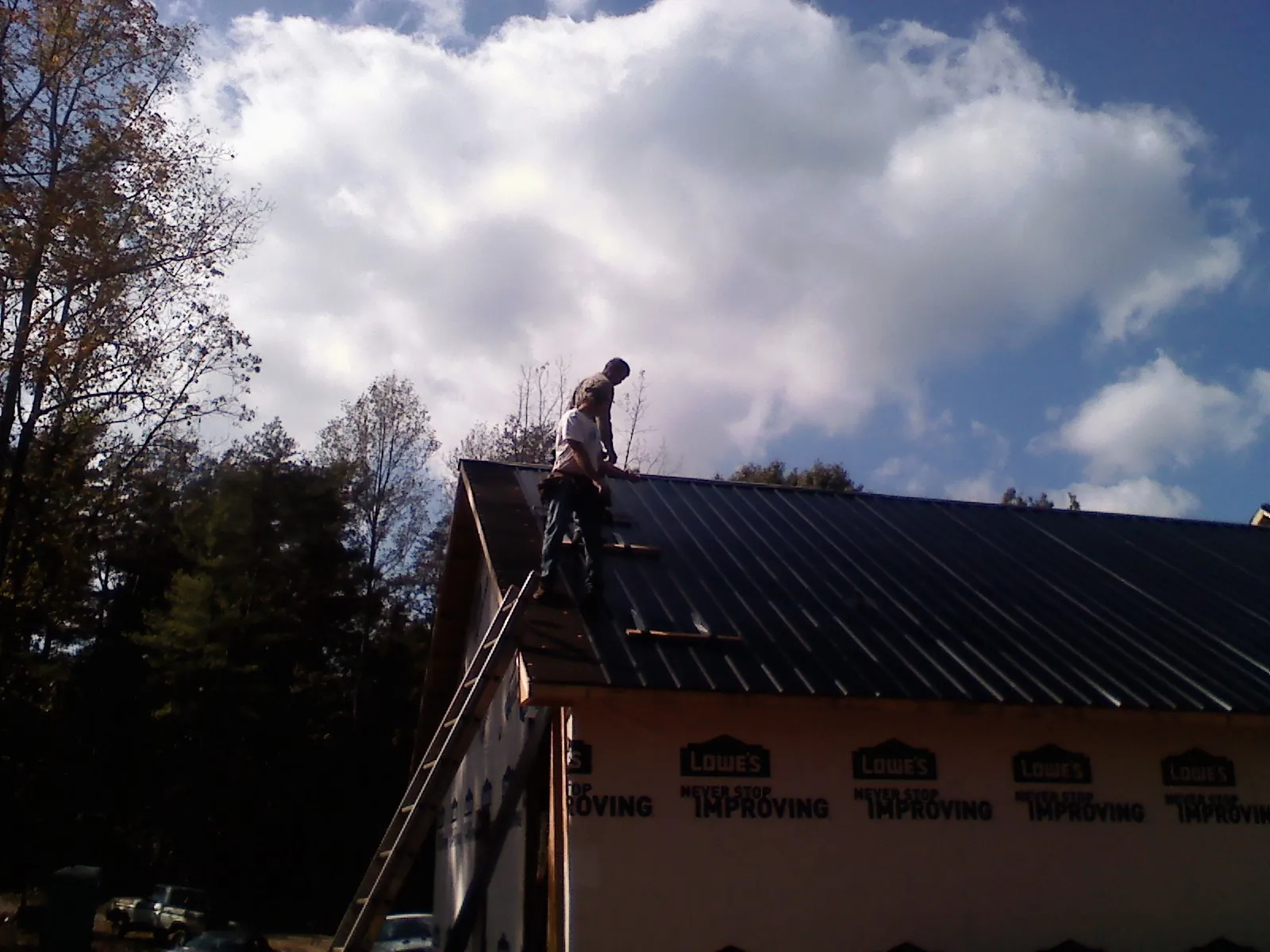 Roofer fastening dark metal panels high against a cloudy sky, from a Roof Inspection job in Quinault