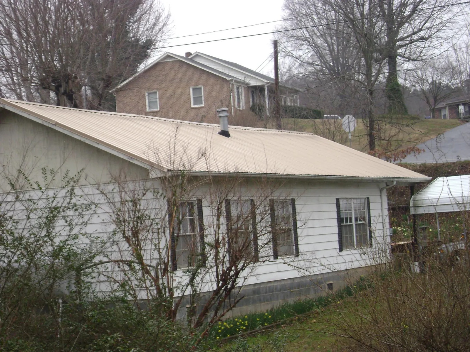 Tan metal roof on a white sided house set into a hillside — Commercial Roofing by Roofing Brothers in Quinault